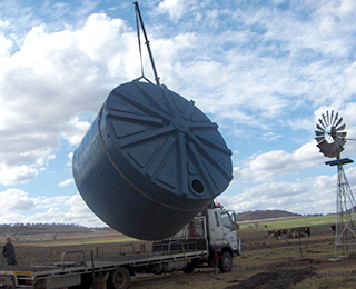 Delivery truck with crane lifting large water tank.